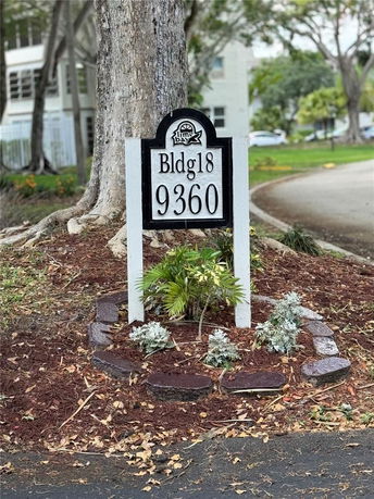 A sign displaying 'Bldg 18' and '9360' in front of a tree, with building structures visible in the background.