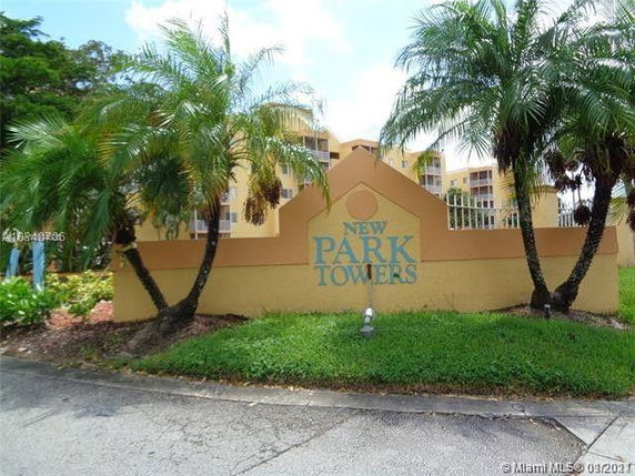 Front view of a residential building labeled 'New Park Towers' with palm trees and a tan exterior.
