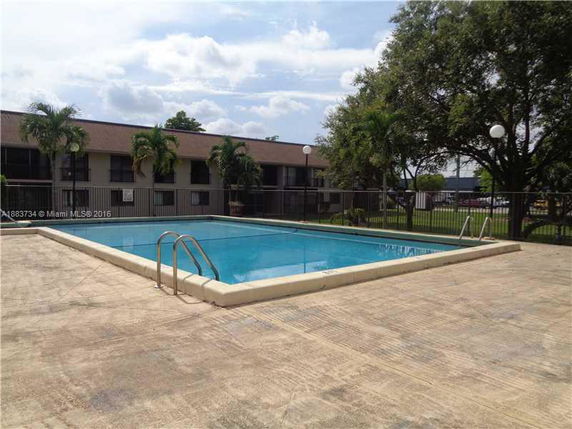 Outdoor swimming pool with surrounding fence and building in the background.