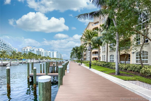 Waterfront walkway with residential buildings and boats docked along the shore.