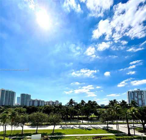 Daytime view of high-rise buildings and greenery under a bright blue sky.
