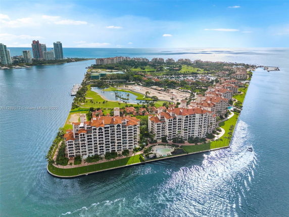 Aerial view of a coastal area with several large, multi-story buildings with red-tiled roofs, surrounded by water and green spaces.