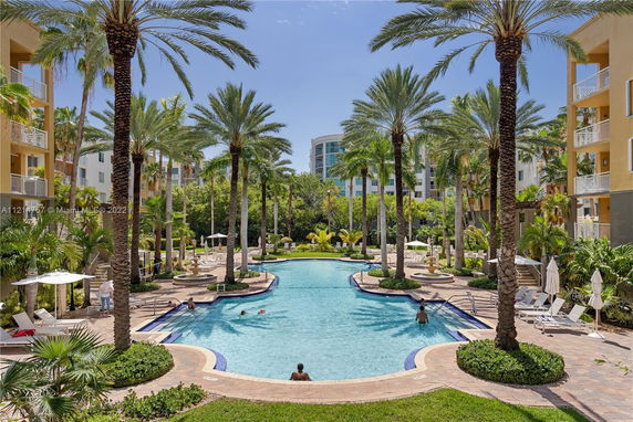 Outdoor swimming pool surrounded by palm trees and apartment buildings.