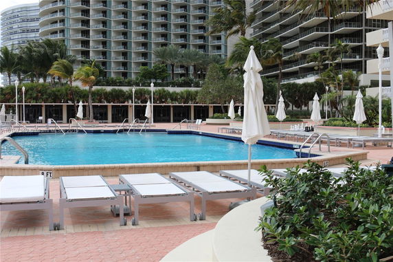 Outdoor pool area with lounge chairs and high-rise buildings in the background.