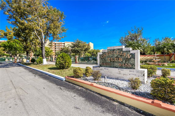 View of the Castillian Club sign and surrounding area with trees and road.
