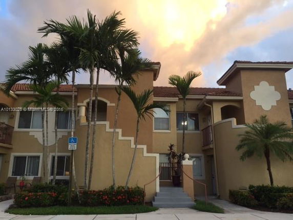 Front view of a two-story residential building with palm trees and a staircase entrance.