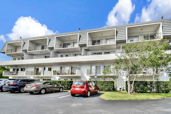 Front view of a residential apartment building with multiple balconies and a parking area.