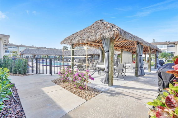 Outdoor area with a thatched-roof pergola and seating next to a swimming pool.