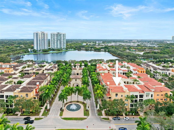 Aerial view of residential buildings with red roofs and tree-lined streets, adjacent to a large lake.