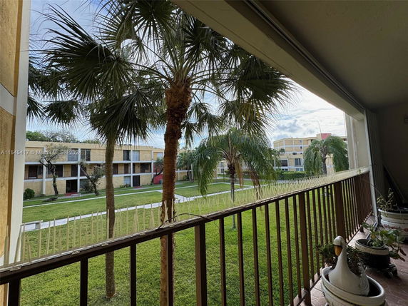 View from a balcony overlooking a courtyard with palm trees and a multi-story residential building in the background.