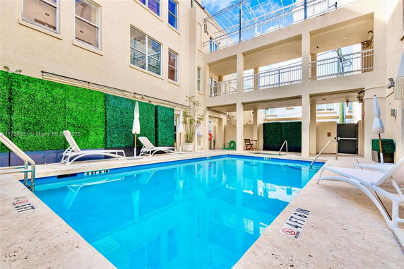 Outdoor swimming pool area adjacent to a building with lounge chairs and greenery.