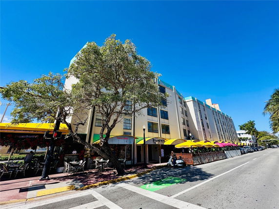 Front view of a multi-story building with sidewalk cafes and colorful awnings.