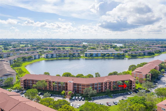 Panoramic view of an apartment complex with a lake and surrounding greenery.