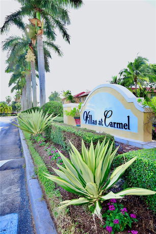 Front view of a sign for Villas at Carmel with palm trees and landscaping.