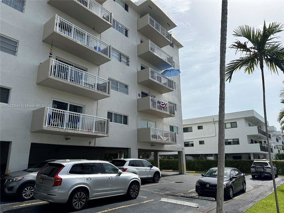 Front view of a multi-story apartment building with balconies and parking space.