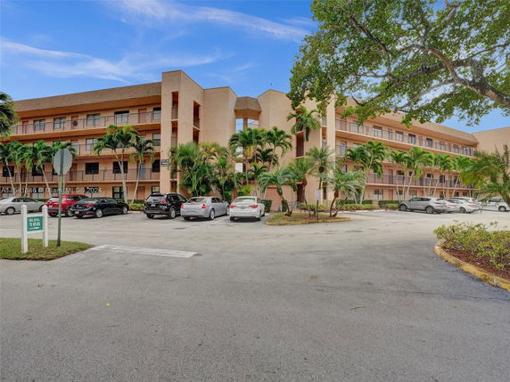 Front view of a multi-story residential building with balconies and surrounding palm trees.
