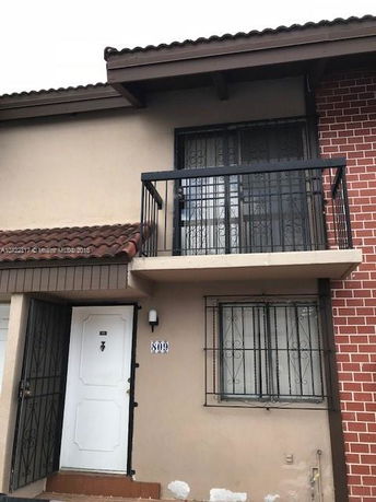 Front view of a two-story house with a balcony and brick wall.