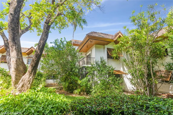 Side view of a two-story house with a balcony and tiled roof surrounded by greenery.