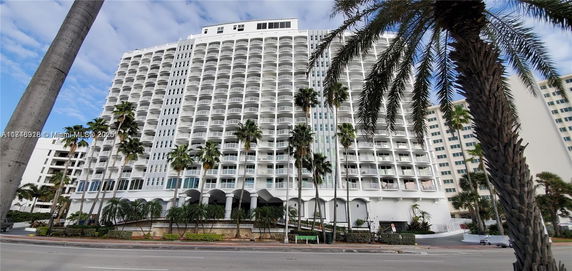Front view of a multi-story building with numerous balconies and palm trees in front.
