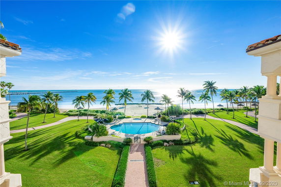 Panoramic view overlooking a landscaped area with a pool, leading to a beach and ocean.