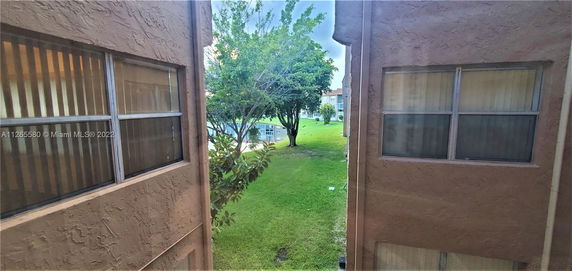 View between two building facades showing windows and green lawn with trees in the background.
