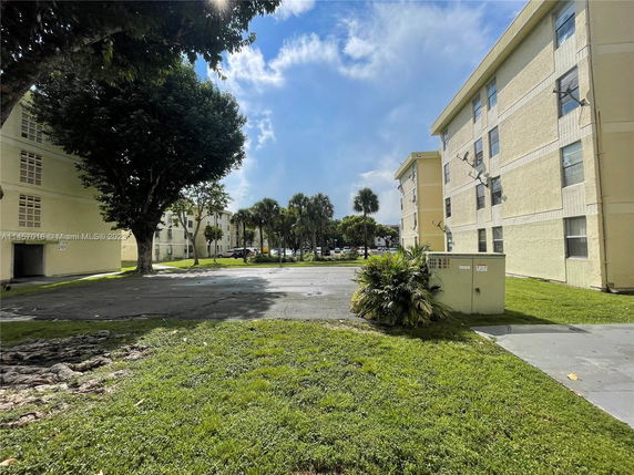 View of a multi-story residential building with yellow exterior walls and multiple windows surrounded by greenery and trees.