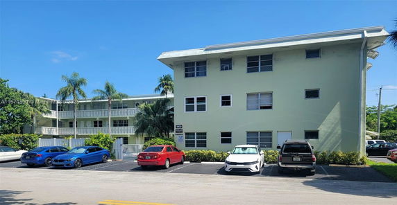 Front view of a multi-story building with parking spaces and several cars.