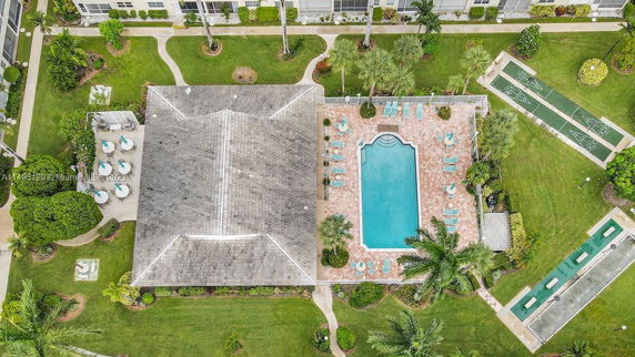 Aerial view of a swimming pool surrounded by a paved area with chairs and tables, next to a building with a gabled roof.