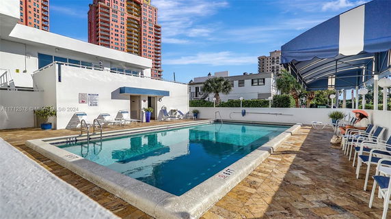 View of an outdoor swimming pool with seating area and building in the background.