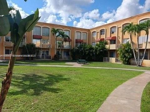 Front view of a three-story apartment building with balconies and green lawn.