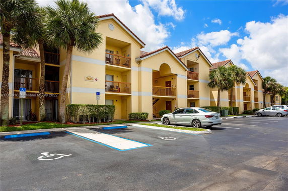 Front view of a multi-story apartment building with balconies and a parking area.