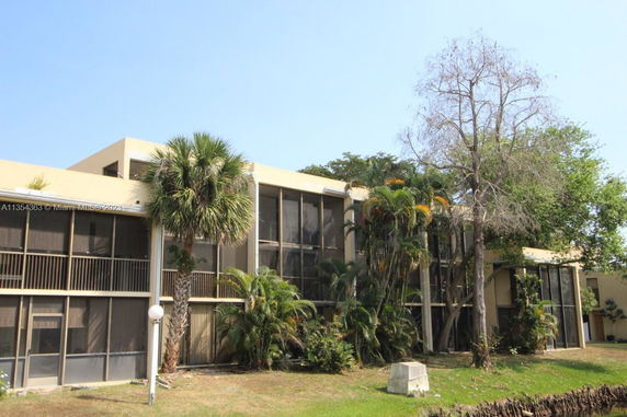 Front view of a multi-story building with screened balconies and surrounding trees.