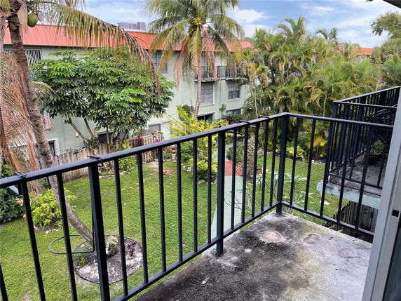 View from a balcony overlooking a green area with palm trees and adjacent residential buildings.