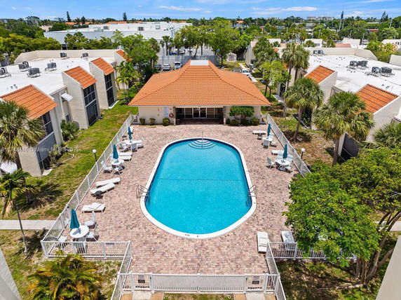 Outdoor swimming pool area surrounded by deck chairs and umbrellas with nearby buildings.
