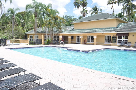 Outdoor swimming pool area with a nearby building and palm trees.
