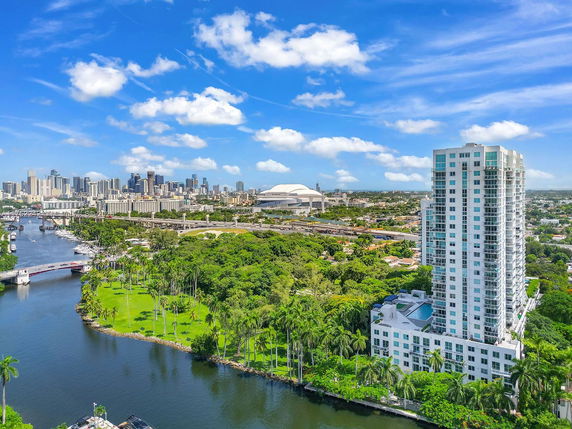 Panoramic view featuring a high-rise building next to a river with a city skyline in the background.