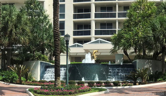 Front view of a multi-story building with balconies and a decorative water fountain in front.