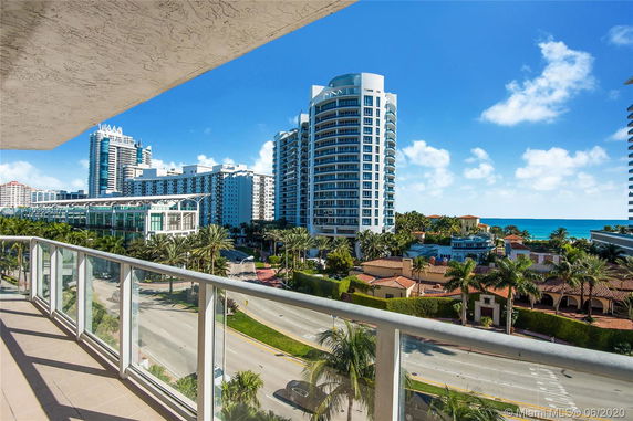 Panoramic view from a balcony overlooking a street and several modern high-rise buildings near the ocean.