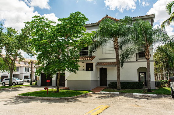 Front view of a two-story residential building with tiled roof and palm trees.
