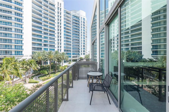 View of modern high-rise buildings with balconies, seen from a balcony with chairs and a table.