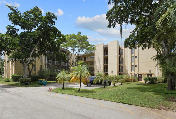 Front view of a multi-story apartment building with balconies and palm trees.