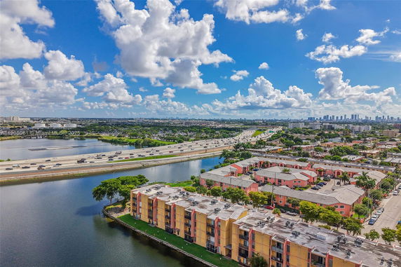 Panoramic view showing buildings, a highway, and a body of water beneath a cloudy sky.