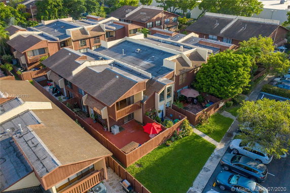 Aerial view of a residential complex with multiple two-story buildings, fenced patios, and surrounding greenery.