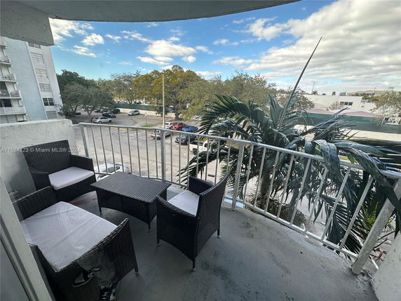 View from a balcony with outdoor furniture overlooking a parking area and nearby buildings.