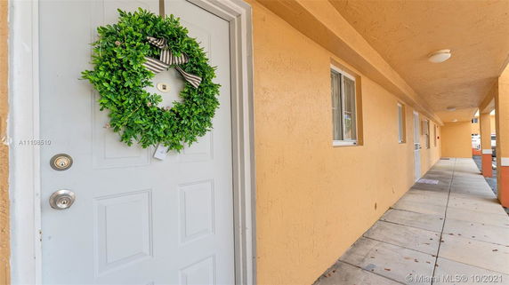 Exterior corridor of a building with a door decorated with a green wreath and beige walls.