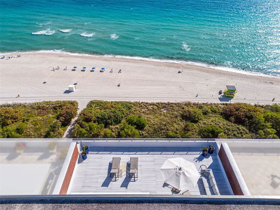 View from a building showing a rooftop area with chairs and umbrellas, overlooking a beach and ocean.