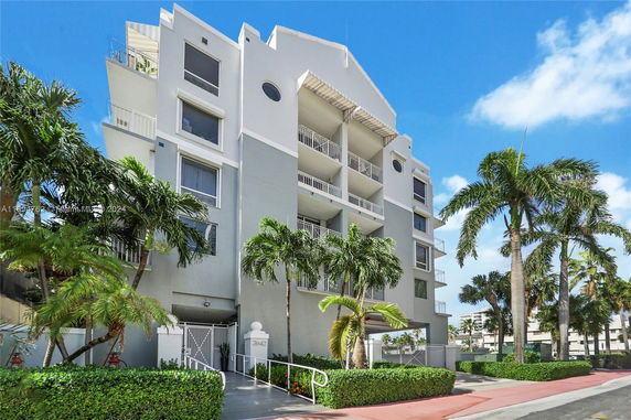 Front view of a multi-story building with balconies and palm trees.