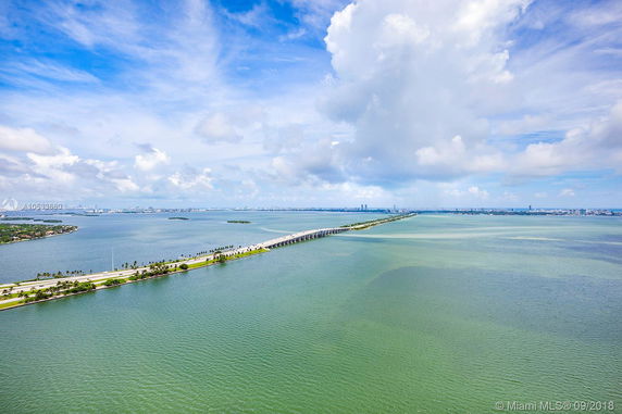 Panoramic view of a long bridge stretching across a body of water with cityscape in the background.