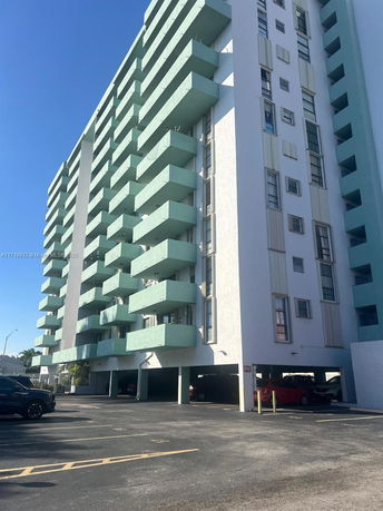 Front view of a multi-story residential building with balconies and a parking area beneath.