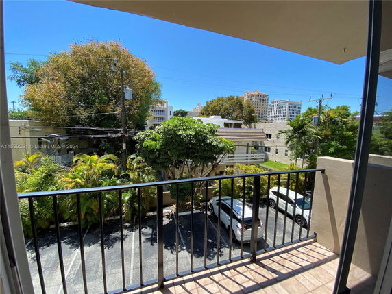 View from a balcony overlooking a parking area with trees and buildings in the background.